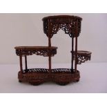 A Chinese hard wood three tier display stand of oval form on six pierced bracket feet