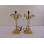 A pair of gilt metal and cut glass table lamps with scrolling arms on raised square bases