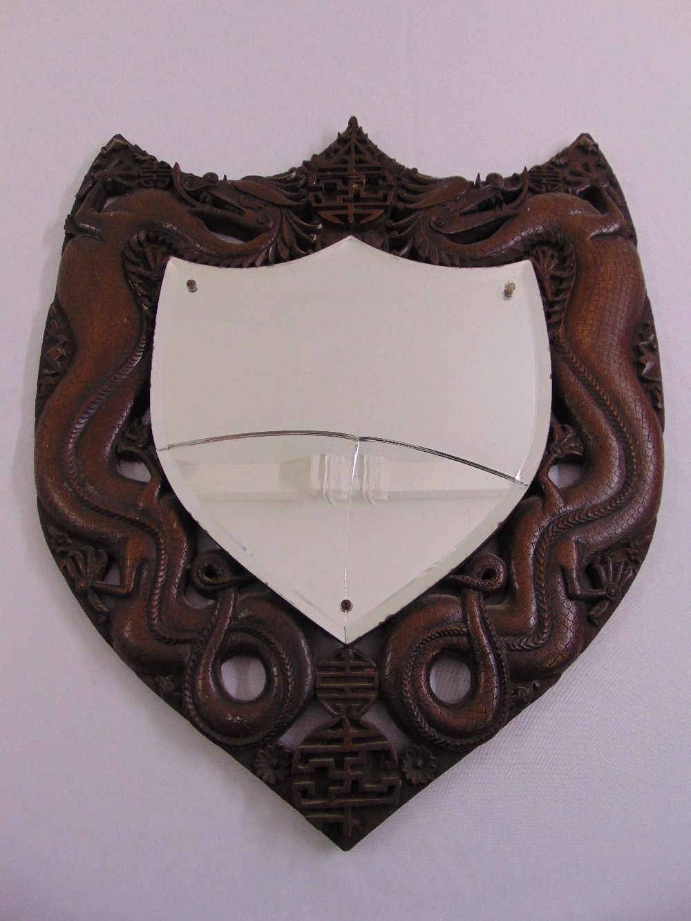 A Chinese shield shaped wall mirror, the pierced hardwood frame carved with dragons, mirror A/F