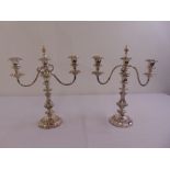 A pair of ornate silver plated two branch candelabra on raised circular bases with detachable