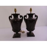 A pair of classical style bronzed lamp bases, with rams head side handles and applied figures in