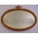 A gilded neo-classical style oval mirror surmounted by an urn with husk swags
