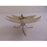A continental white metal fruit stand of leaf form with applied bird on three scroll supports