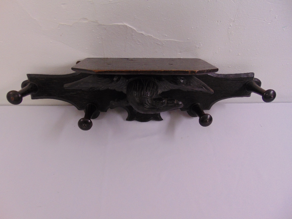 An ebonised hat and coat wall mounted stand decorated with a carved eagle
