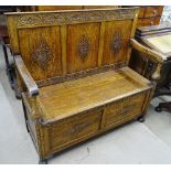 A 1920s carved and panelled oak settle, with risin