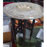 An Eastern embossed brass top table on folding bas