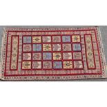 Sozani woollen rug, the grid field having coloured square dispersed with red, within a boteh border,