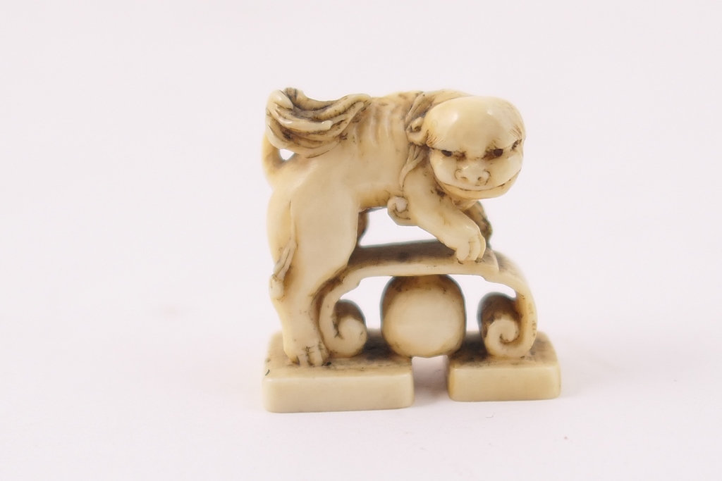 Japanese carved ivory netsuke, Meiji (1868-1912), carved as a shi-shi dog with bench and ball,