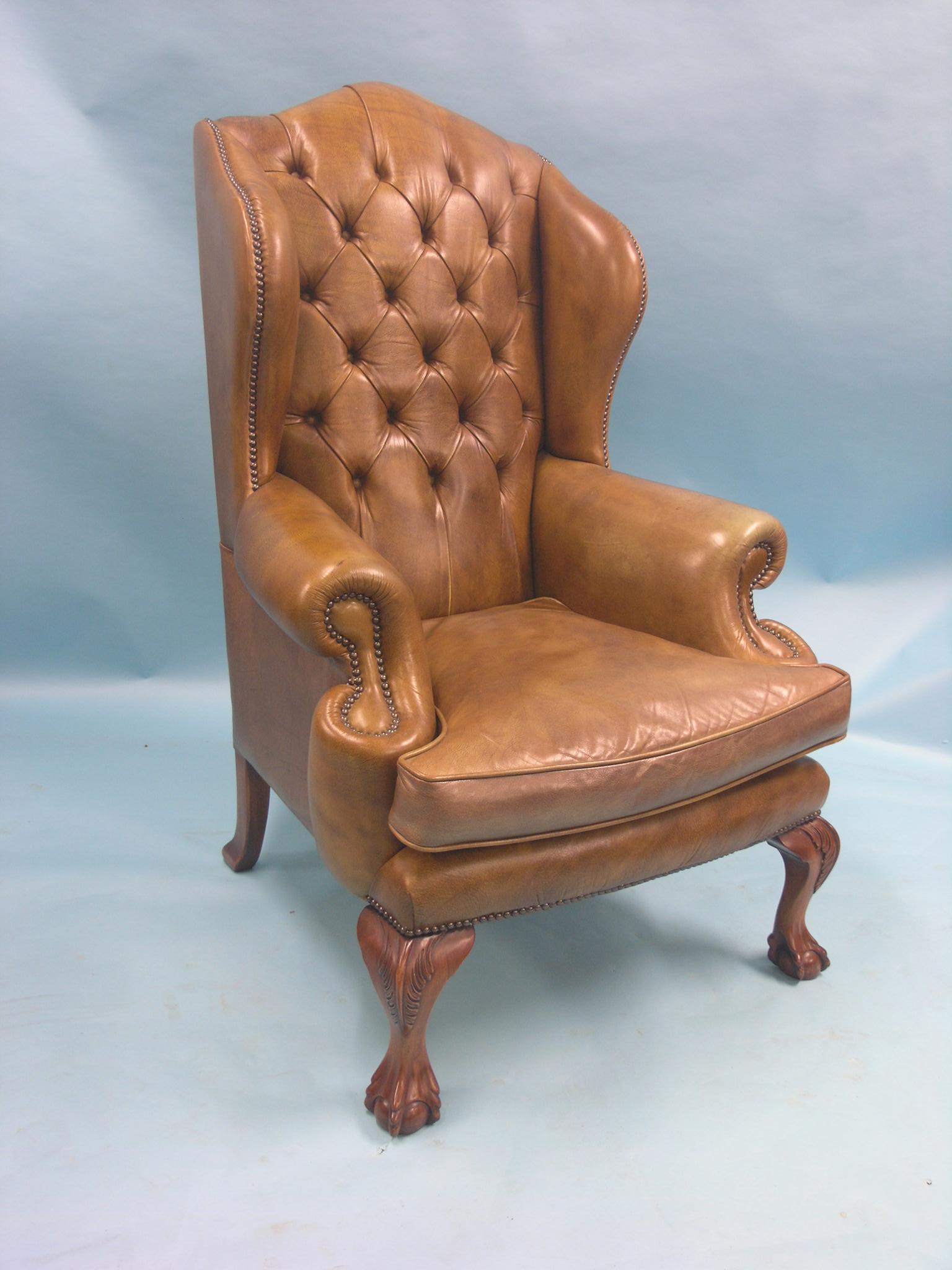 A Reprodux Chippendale-style wing armchair, upholstered in a buttoned olive leather, on carved front