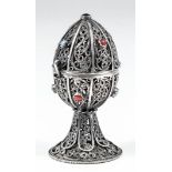 A Russian silvery metal filigree egg pattern ornament with pierced scroll panels and inset with