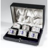 A set of six George V silver napkin rings with leaf and floral cast mounts and enamelled with two