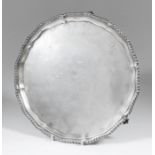 A late Victorian silver circular salver, the shaped and moulded rim with gadroon mounts and on three