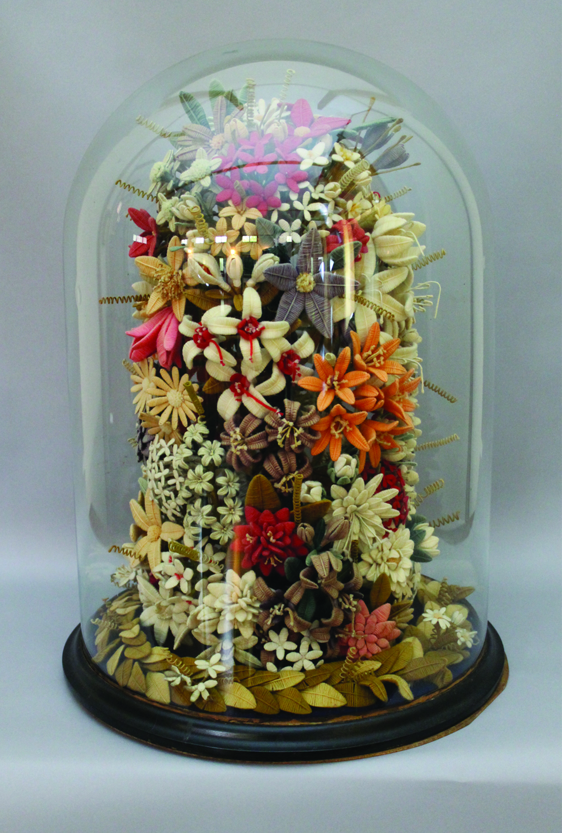 A Victorian woolwork mixed floral display contained in a cylindrical glass dome, with turned