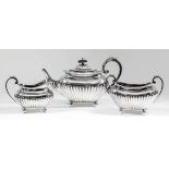 An Edward VII silver rectangular three piece tea service with reeded mounts, part reeded domed cover