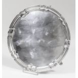 A George V silver circular salver with shaped and moulded rim, on three scroll and hoof pattern