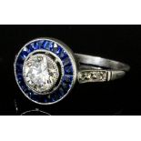 A 1920's silvery coloured metal mounted diamond and sapphire circular "halo" ring, the collet