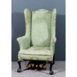 A wing back easy chair of 18th Century design, upholstered in green brocade on shell capped cabriole