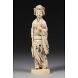 A JAPANESE MEIJI PERIOD ONE PIECE CARVED IVORY BIJIN FIGURE, her hair elegantly coiffured, her robes