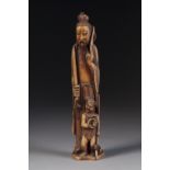 AN AGED CHINESE ONE PIECE CARVED IVORY FIGURE OF A BEARDED DEITY HOLDING A SWORD, a smaller figure