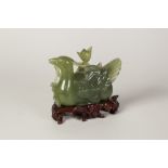 AN EARLY TWENTIETH CENTURY CHINESE CARVED GREEN HARDSTONE RECUMBENT DUCK, holding a lotus plant in