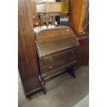 1930's OAK BUREAU WITH CURVED SHOULDERS, TWO LONG DRAWERS BELOW, ON CUP AND COVER SUPPORTS AND SEDGE