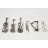 FIVE MINIATURE WHITE METAL MUSICAL INSTRUMENTS AND ANOTHER WHITE METAL STAND (6)