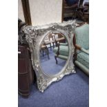 MODERN OVAL BEVELLED EDGE WALL MIRROR IN ORNATE SILVERED FOLIATE AND SHELL PATTERN FRAME