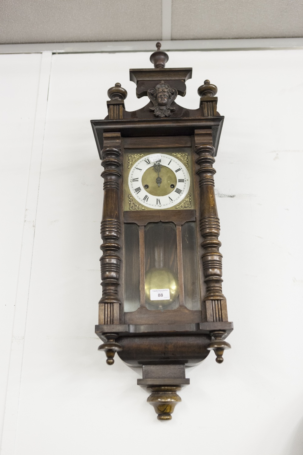 A VIENNA WALL CLOCK, BRASS FACE WITH CREAM CHAPTER RING, BLACK ROMAN NUMERALS, TYPICAL CASE WITH