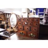 A SOLID WOOD MINIATURE CHEST OF 14 VARIOUS SIZED DRAWERS AND A SMALL OVAL DRESSING TABLE MIRROR (2)