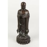 A CHINESE QING DYNASTY PATINATED BRONZE FIGURE OF A BUDDHISTIC DISCIPLE , holding in his left hand a