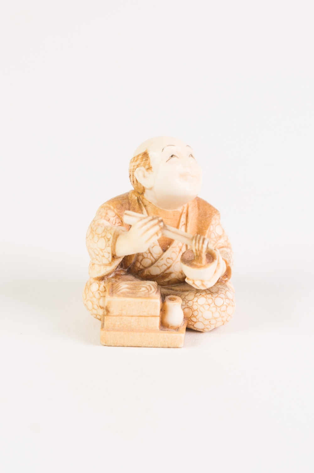 GOOD JAPANESE MEIJI PERIOD CARVED AND, IN PART, LIGHTLY STAINED IVORY NETSUKE OF A SMILING MAN