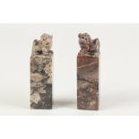 A NEAR PAIR OF CHINESE MOTTLED PURPLISH HARDSTONE SQUARE SEALS, surmounted with Buddhistic lions,