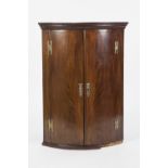 GEORGE III FLAME CUT MAHOGANY BOW FRONTED CORNER CUPBOARD, of typical form with moulded cornice,