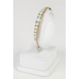 EDWARDIAN (UNMARKED) GOLD HINGE OPENING BANGLE, the top set with fifteen opals, graduating from