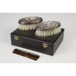 MODERN CASED PAIR OF EMBOSSED SILVER BACKED MILITARY HAIR BRUSHES, of oval form with scroll