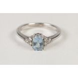 9ct WHITE GOLD RING, with an oval blue topaz in a four claw setting, each shoulder having a trio