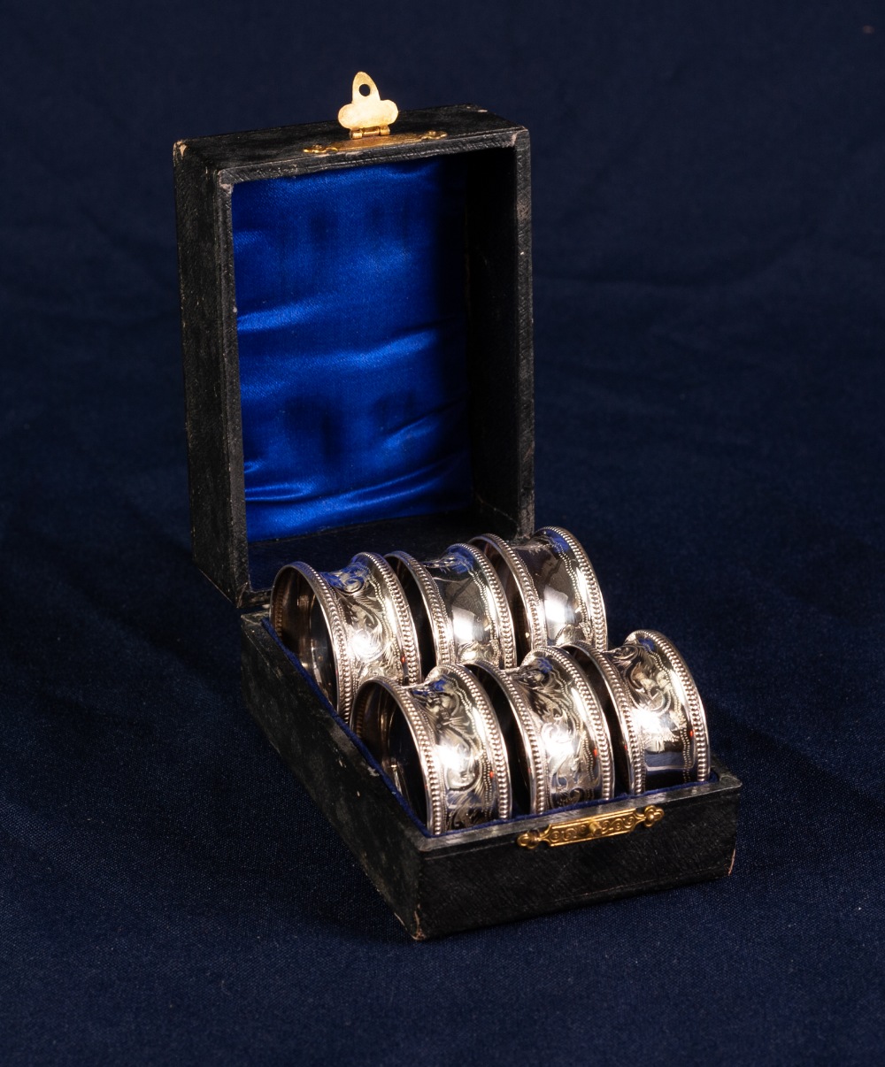 EARLY 20th CENTURY CASED SET OF SIX SILVER NAPKIN RINGS with beaded borders and foliate scroll