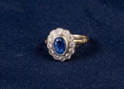 18ct GOLD, SAPPHIRE AND DIAMOND CLUSTER RING, collet set with an oval sapphire and surround of