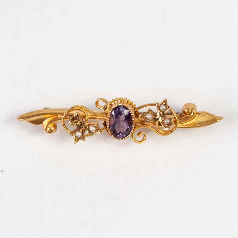 AN EDWARDIAN 15ct GOLD FOLIATE SCROLL BAR BROOCH, collet set with a centre oval amethyst, and two