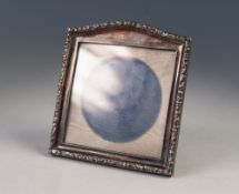 AN EASEL PHOTGRAPH FRAME with silver rectangular front with low arched top, rococo embossed