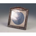 AN EASEL PHOTGRAPH FRAME with silver rectangular front with low arched top, rococo embossed