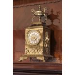 A BRASS MANTEL CLOCK WITH URN SURMOUNTING, ENAMELLED NUMERALS TO THE BRASS DIAL, 1'5" HIGH