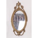 AN OVAL WALL MIRROR WITH GILT FRAME WITH URN AND FESTOON PEDIMENT AND FESTOON BASE