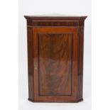 EARLY NINETEENTH CENTURY FIGURED MAHOGANY FLAT FRONTED CORNER CUPBOARD, the moulded cornice above