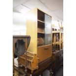 A TEAK BOOKCASE WITH TWO GLASS SLIDING DOORS AND FALL-FRONT COMPARTMENT BELOW, A TEAK BOOK RACK