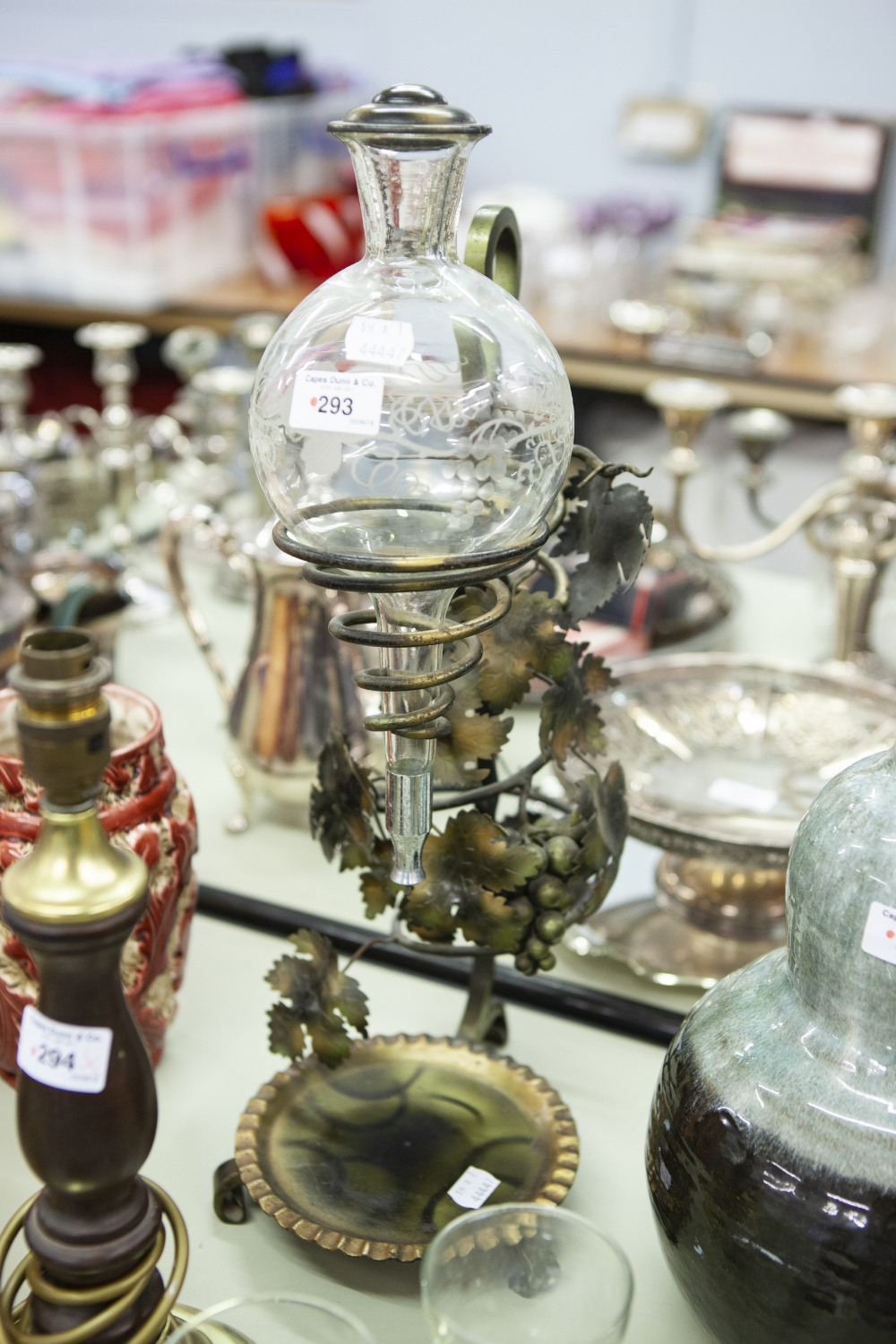 A GREEK WINE DISPENSER, A GLASS RECEPTACLE ON METAL DECORATIVE STAND