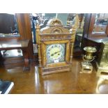AN OAK CASED MANTEL CLOCK WITH SHAPED TOP, GLAZED DOOR ENCLOSING SILVERED CHAPTER RING AND BLACK