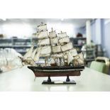 A SMALL MODEL OF A THREE MASTED SAILING SHIP UNDER SAIL, ON STAND