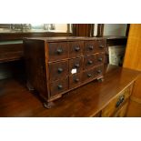 AN OAK MINIATURE TABLE TOP CHEST OF DRAWERS, TWELVE BOX DRAWERS WITH TURNED HANDLES ALL RAISED ON