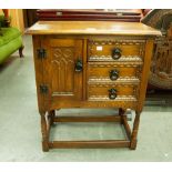 AN OAK SMALL CABINET WITH THREE DRAWERS AND A CUPBOARD WITH CARVED DECORATION TO THE FRONT